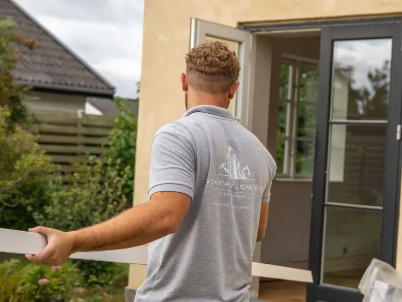 Christian Schucany bærer en lang hvid liste ind gennem terrassedøren på en pudset villa