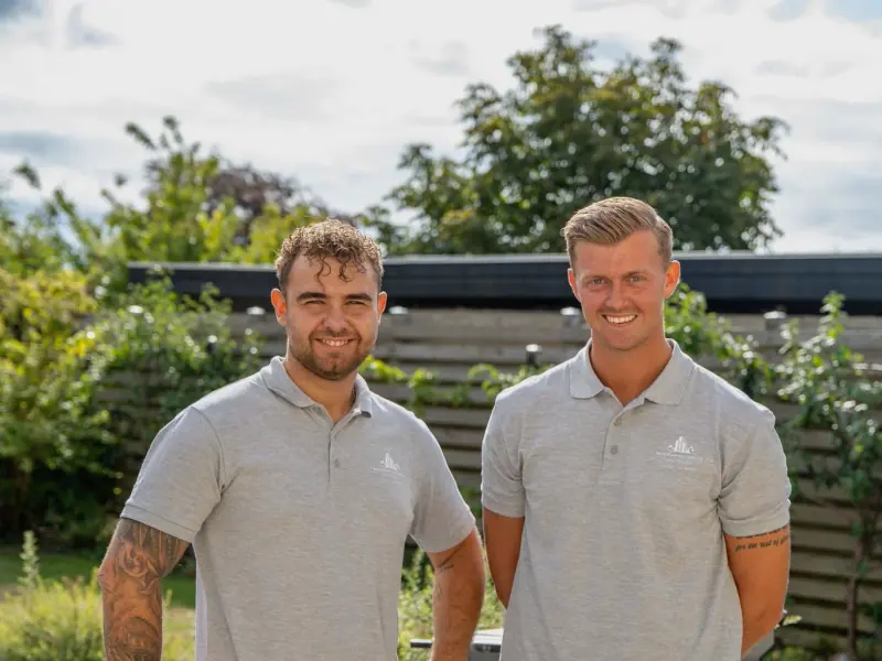 Christian Schucany og Mikkel Birch Cartey side om side i firmapolo på en arbejdsplads i en have
