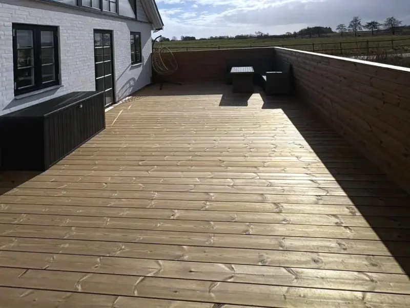Hævet træterrasse langs husgavl med stort trekantet vinduesparti